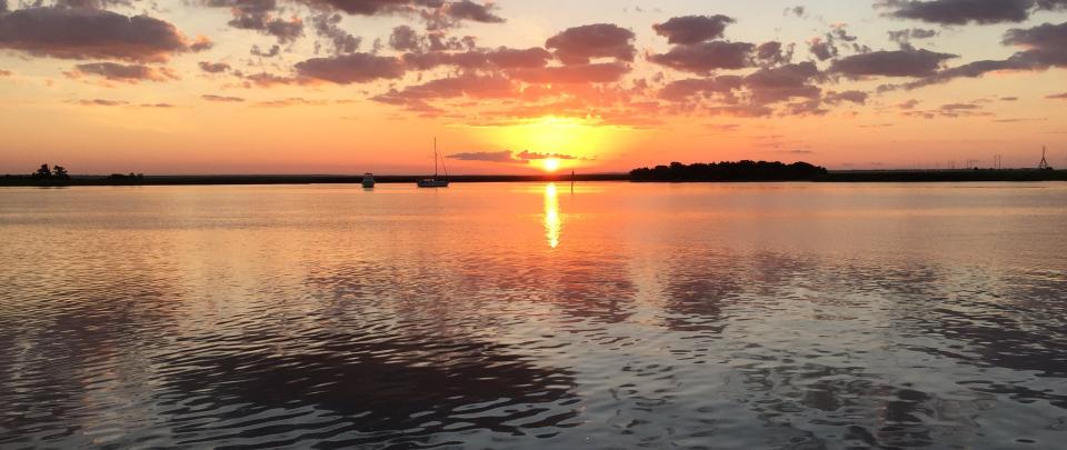 an orange sun sets over calm water 