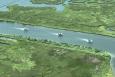 3 boats cruise down a river surrounded by green marshland