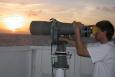 A scientist looking through a large set of binoculars, viewing marine mammals.