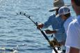 Three anglers on a boat with a fishing rod that's bending and looks to have a fish on.