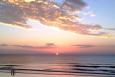 a couple stands on a beach with an orange sunset in the background 