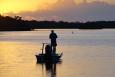 Silhouette of an angler fishing from a small boat on a lake with the sun setting in the background.
