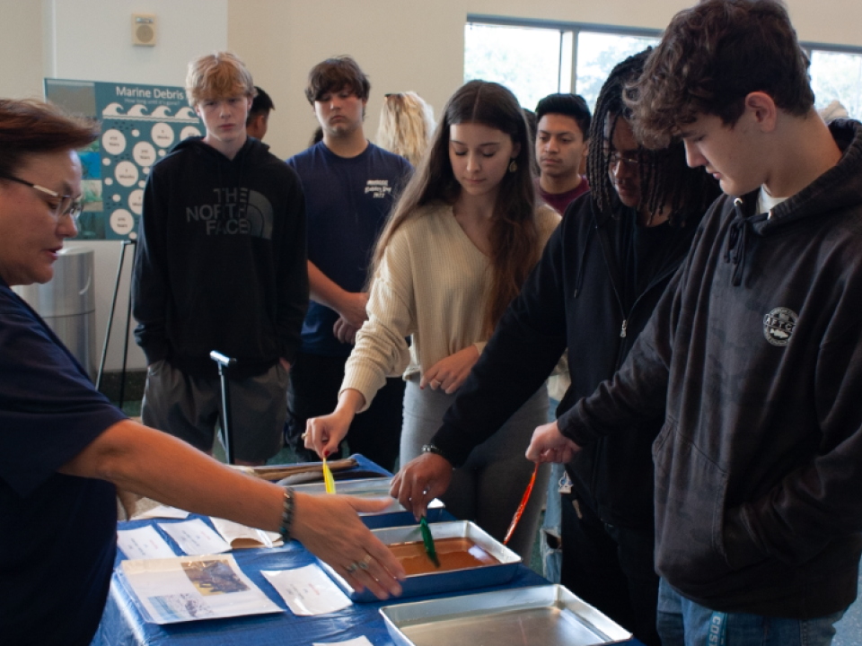 a group of students hold different colored sticks into silver pans