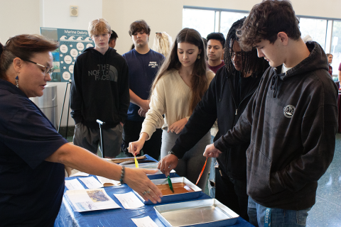 a group of young men and women look at a project on a table