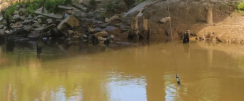 a water quality testing line is lowered from a bridge into brown water 