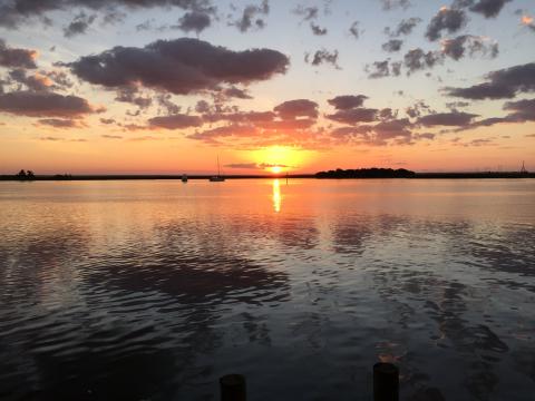 an orange sun sets over calm water 