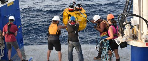 a crew on a boat helps retrieve a piece of equipment out of the water 