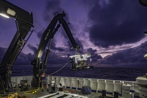 A remotely operated vehicle is lifted onto a ship deck by a large mechanical arm.