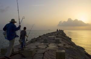 Fishemen walk along a rocky pier.